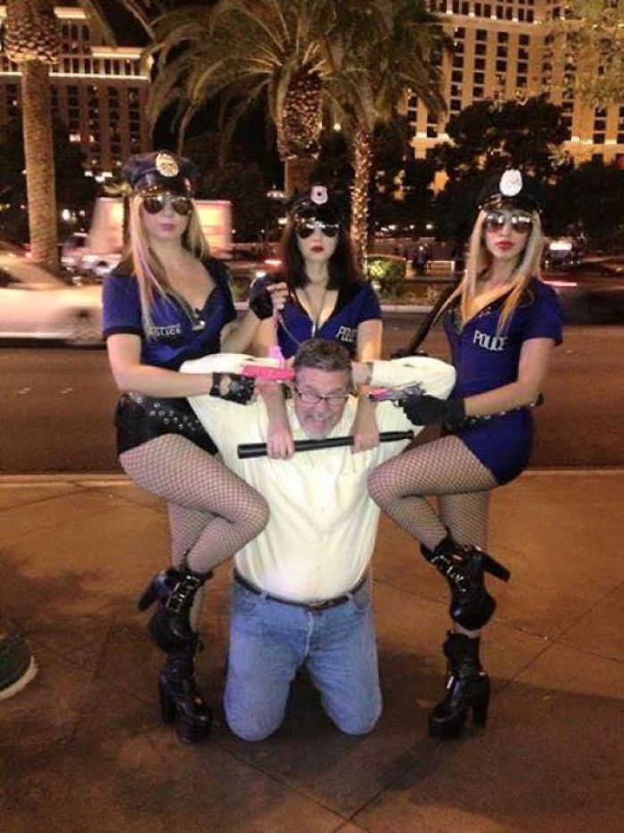 Dad posing humorously with women in police costumes on a city street at night.