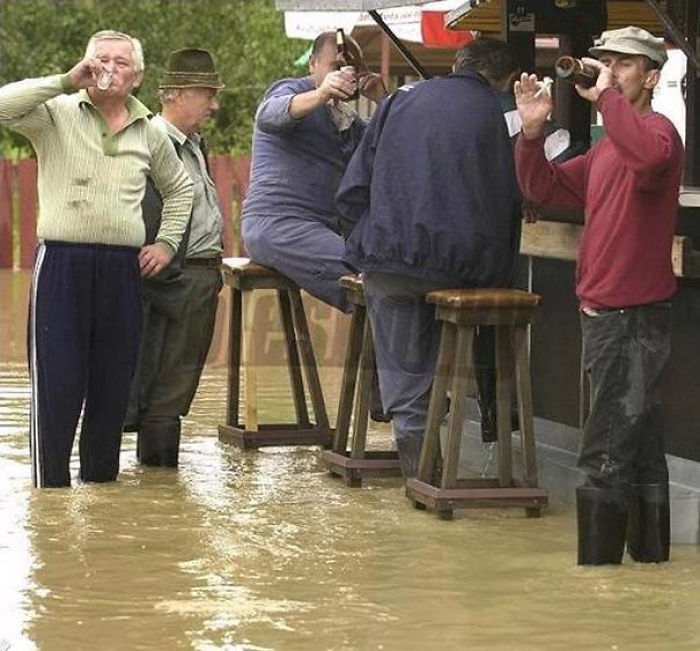 People at an outdoor bar ignore the floodwaters, drinking and standing in knee-high water.