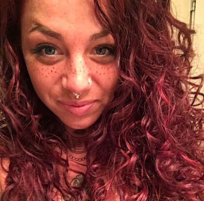 Woman with tattooed freckles, curly red hair, and a septum piercing, showcasing the latest beauty trend.