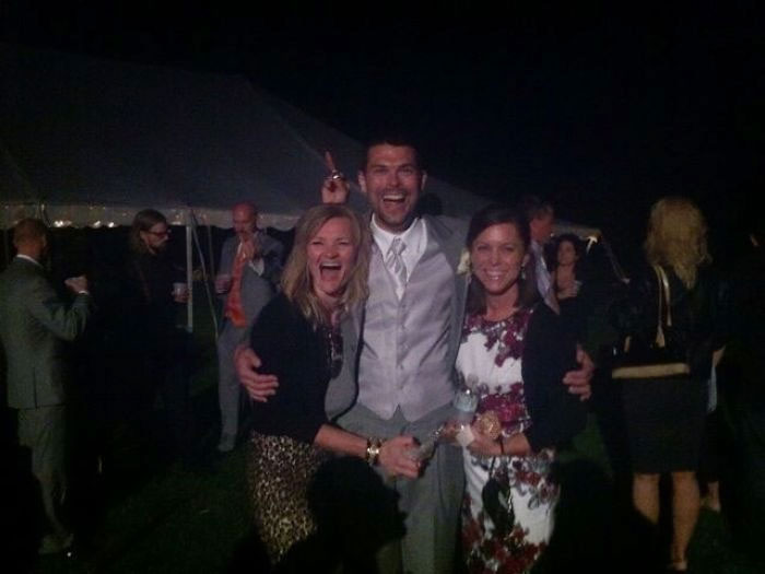 A dad makes funny bunny ears gesture behind friends at an outdoor night event.