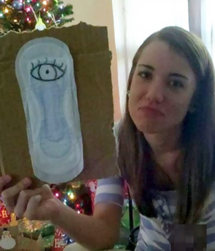 Young woman holding a cardboard with a drawing, displaying a playful dad joke in front of a Christmas tree.