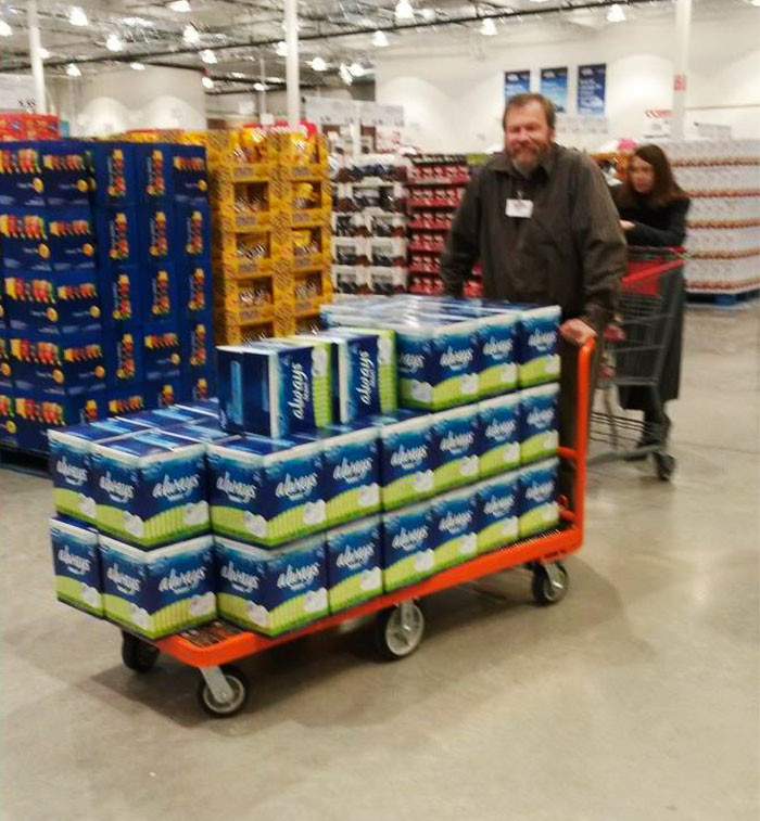Dad humor: a man in a store pushing a cart loaded with an excessive amount of feminine hygiene products.