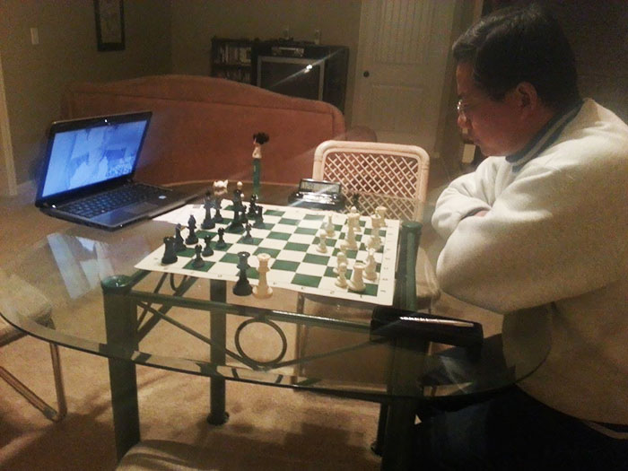 Dad playing chess with a baby monitor while dressed casually, showcasing a humorous approach to parenting.