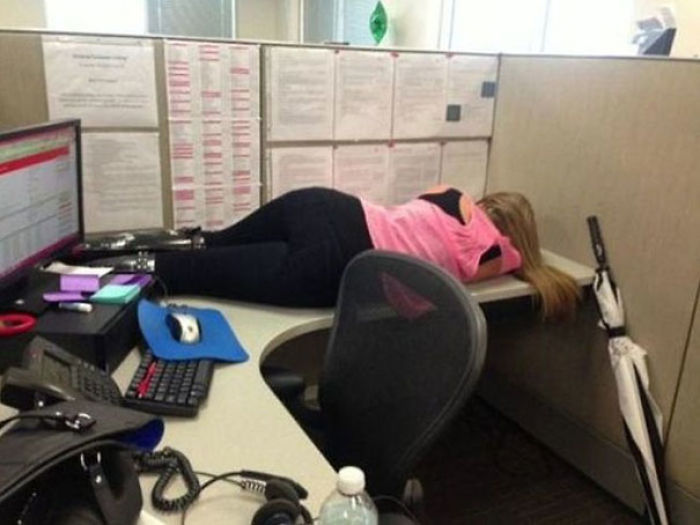 Office worker lying on desk in cubicle, clearly not caring about tasks.