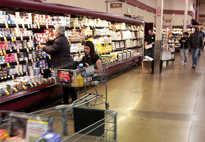 Person sitting in a shopping cart in a grocery aisle, illustrating carefree attitude.