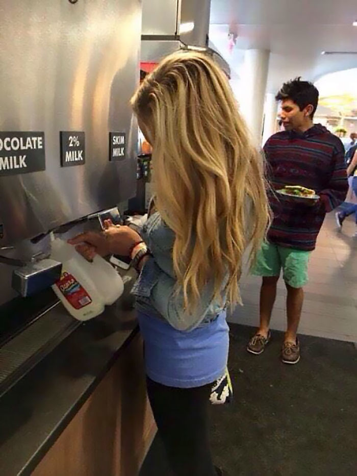 Woman casually filling a gallon jug at a milk dispenser, showing a carefree attitude in a public place.