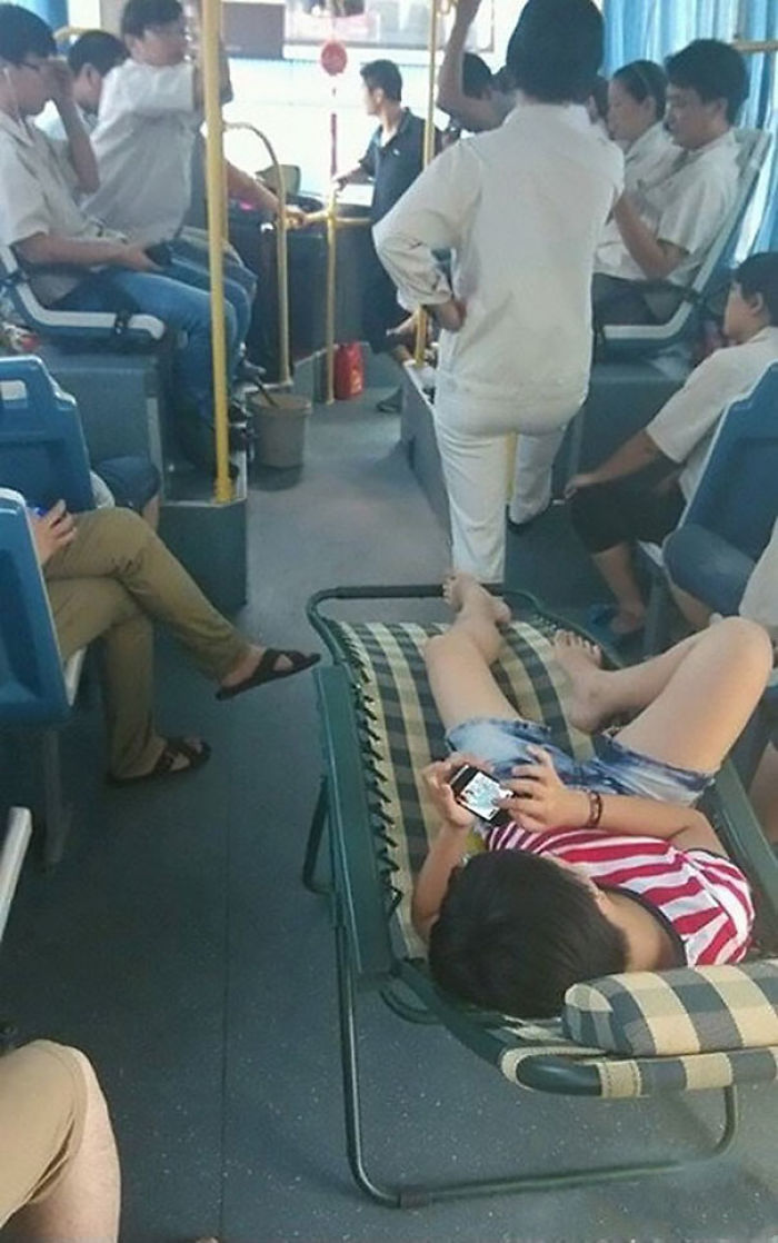 Person lounging on a bus in a hammock, using a phone, while others sit around.