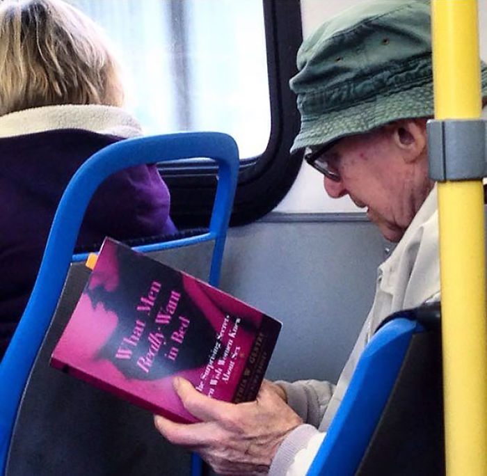 Elderly man reading book on bus, showing indifference to surroundings.