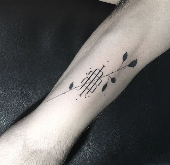 Delicate and sophisticated typographic tattoo on forearm with floral design and geometric lines.