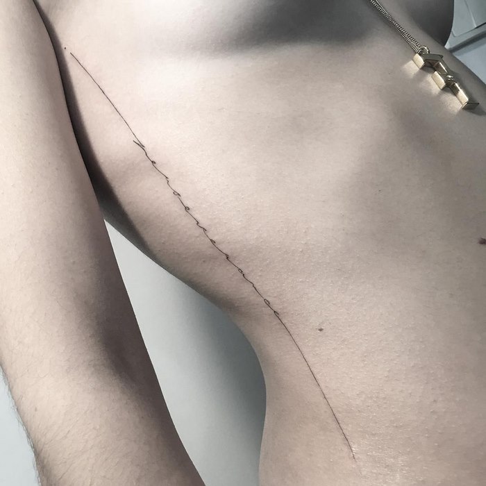 Delicate typographic tattoo by Léo Gavaggio on a person's side, featuring a fine line with subtle details.