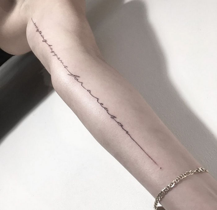 Delicate typographic tattoo on an arm, showcasing simple yet sophisticated design by Léo Gavaggio.