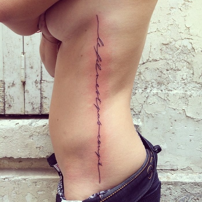 Delicate typographic tattoo in black ink running vertically along a person's ribcage.