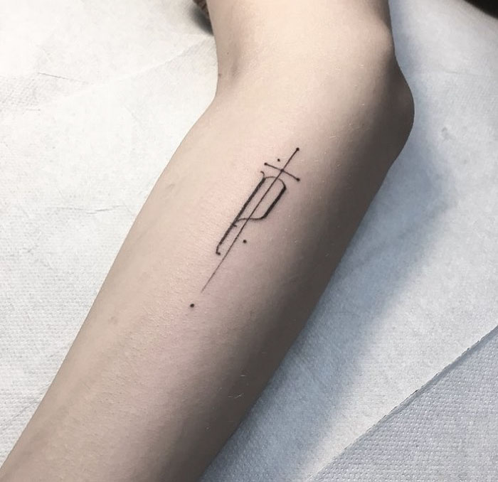 Delicate typographic tattoo by Léo Gavaggio on an arm with geometric design elements.