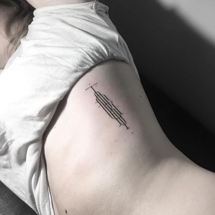 Delicate typographic tattoo by Léo Gavaggio on a person's ribcage, showcasing intricate line work.