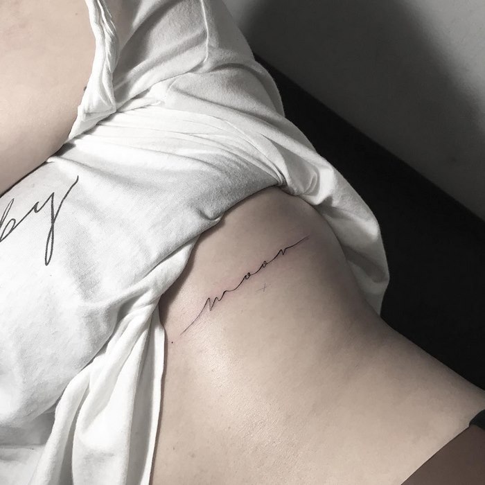 Delicate typographic tattoo by Léo Gavaggio depicting the word "moon" on a person's side.
