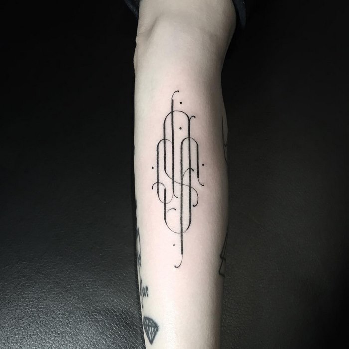 Delicate and sophisticated typographic tattoo in black ink by Léo Gavaggio on a forearm.