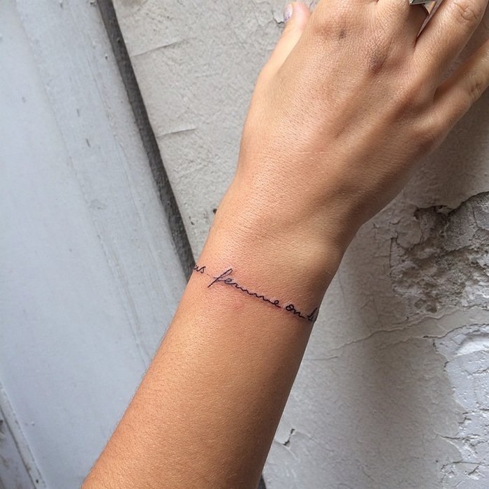 A delicate typographic tattoo by Léo Gavaggio wraps around a wrist, showcasing elegant and sophisticated style.