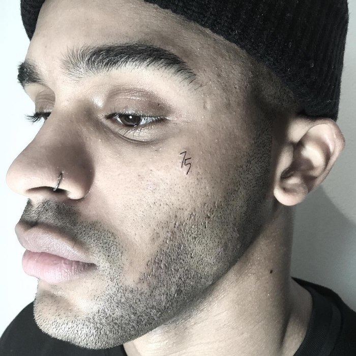 Close-up of a man with a delicate typographic tattoo on his cheek, featuring minimalistic design elements.