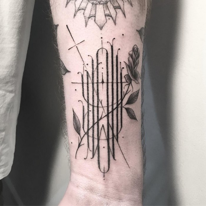 Delicate typographic tattoo featuring floral elements on an arm, showcasing a sophisticated design by Léo Gavaggio.