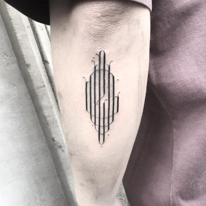 Delicate typographic tattoo by Léo Gavaggio on forearm, featuring intricate lines and shapes.