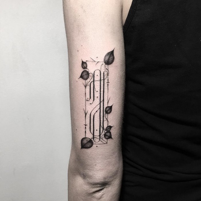 Delicate and sophisticated typographic tattoo with leaf motifs on an arm.