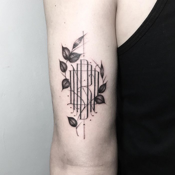 Delicate and sophisticated typographic tattoo by Léo Gavaggio, featuring intricate lettering and leaf designs.