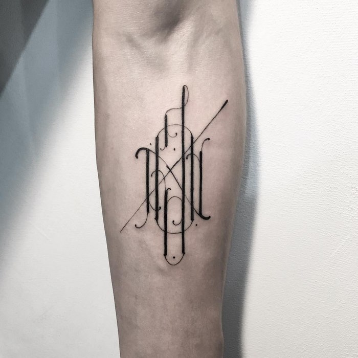 Delicate typographic tattoo on forearm by Léo Gavaggio, featuring intricate black linework.
