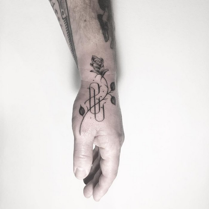 Hand with a delicate typographic tattoo by Léo Gavaggio featuring a rose and elegant script on a light background.