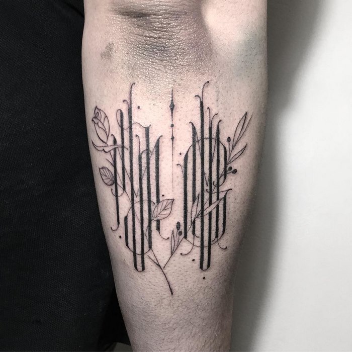 Typographic tattoo by Léo Gavaggio on a forearm, featuring delicate, sophisticated linework and floral elements.