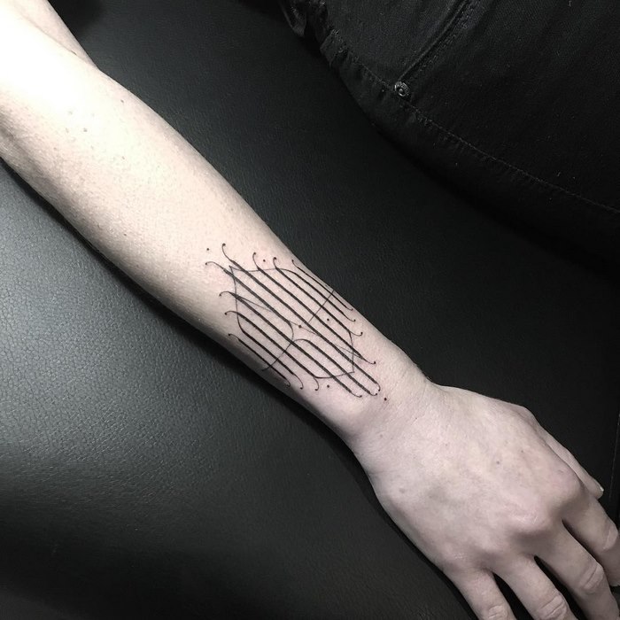 Delicate and sophisticated typographic tattoo on a person's forearm, featuring intricate line design.