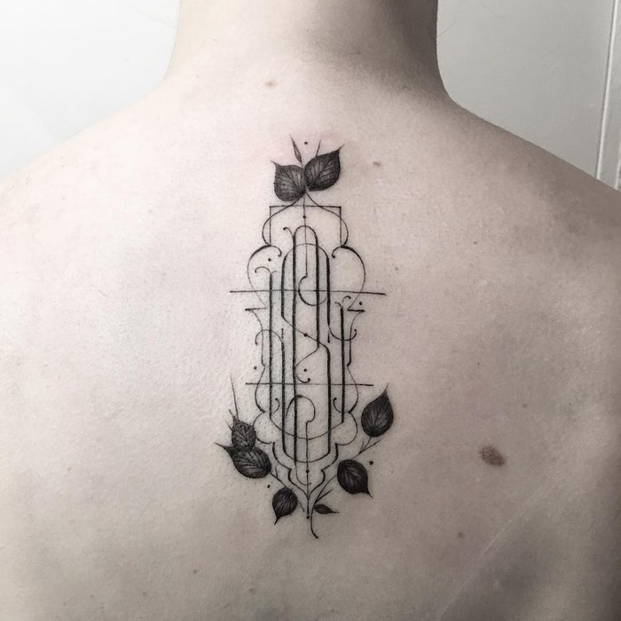 Delicate typographic tattoo on back with intricate lines and leaf designs by Léo Gavaggio.