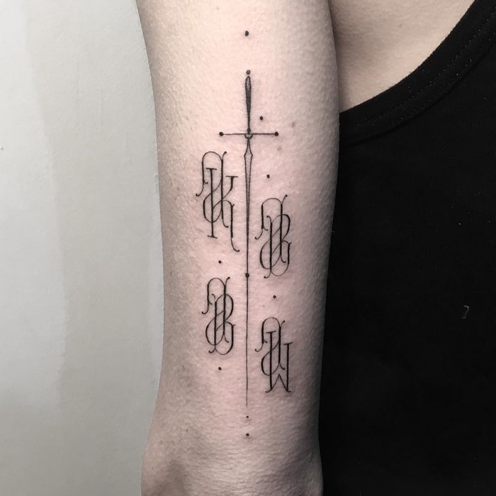 Delicate typographic tattoo by Léo Gavaggio features elegant letters and a sword design on an arm.