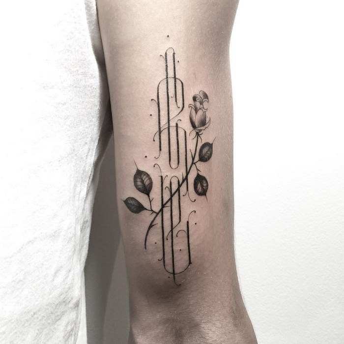 Delicate and sophisticated typographic tattoo with floral elements on an arm.