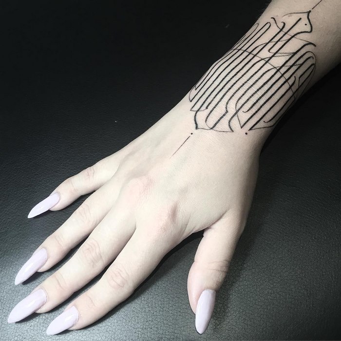 Delicate and sophisticated typographic tattoo by Léo Gavaggio on a person's forearm with light purple nails.