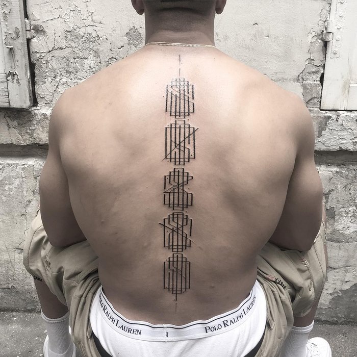 Back view of a person with a delicate and sophisticated typographic tattoo along the spine by artist Léo Gavaggio.