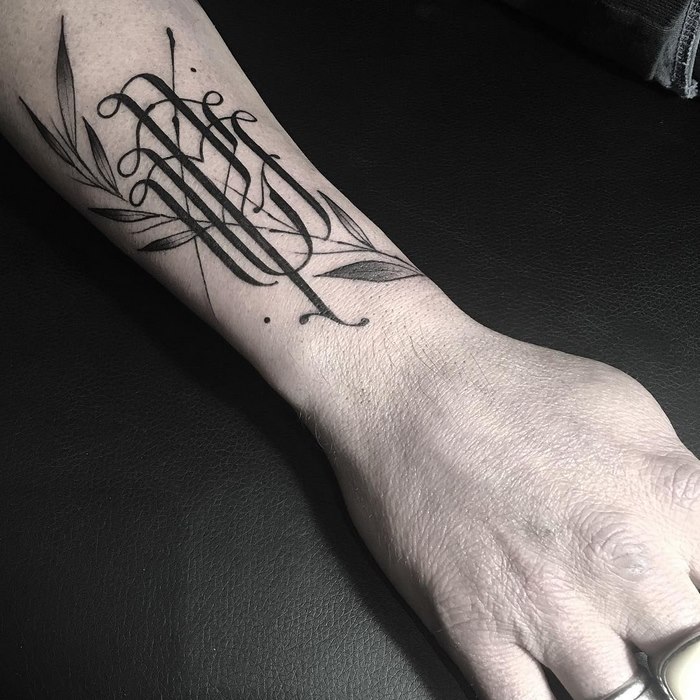 Elegant typographic tattoo by Léo Gavaggio, featuring delicate script intertwined with leaf motifs on a person's forearm.