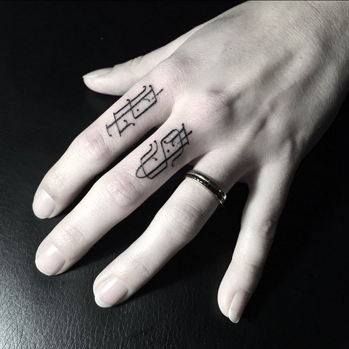 Delicate typographic tattoo on fingers, showcasing sophisticated design in black ink.