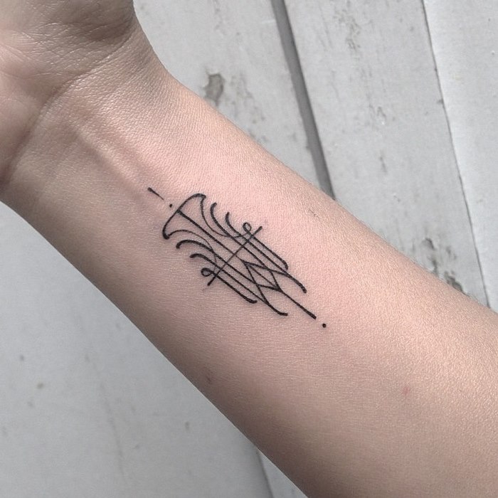 Delicate, sophisticated typographic tattoo on an arm, featuring intricate linework by Léo Gavaggio.