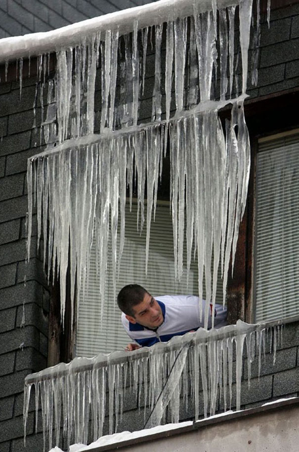 Man peering out window with large icicles, illustrating why women live longer than men in risky situations.