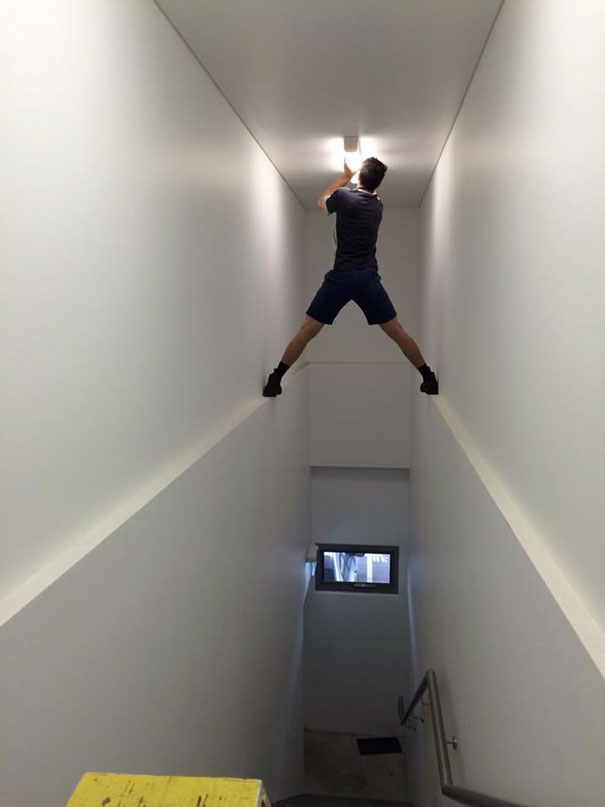 Man standing precariously on walls to change light bulb, illustrating why women live longer.