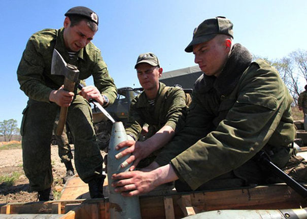 Three men in military uniforms working together, handling what appears to be artillery in an outdoor setting.