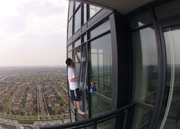 Man precariously cleaning a high-rise window without safety gear, illustrating why women live longer than men.