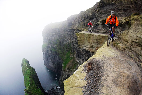 Two cyclists ride along a narrow cliff edge, demonstrating risk-taking behaviors related to lifespan differences between genders.