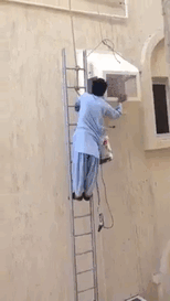 Man balancing on a ladder while fixing a window air conditioner unit.