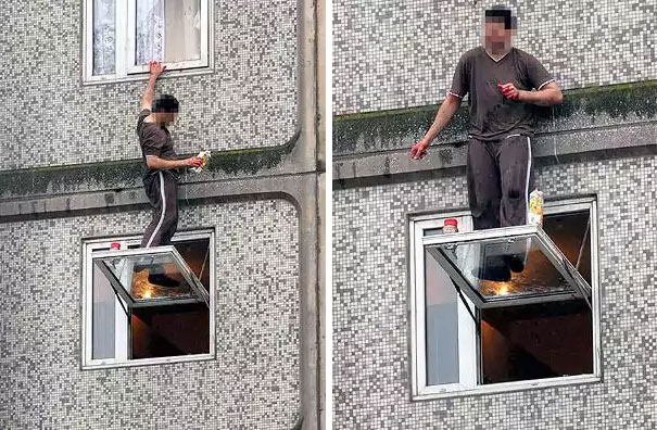 Man precariously standing on an open window ledge of a building, balancing with one hand on the wall.
