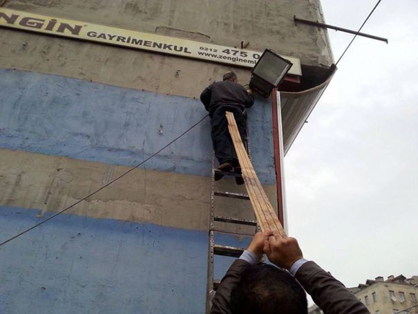 Man precariously balanced on ladder using wooden planks for support, highlighting risky scenarios.