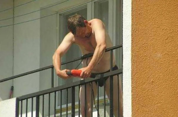 Man using a power tool on a balcony rail, shirtless, demonstrating risky behavior.