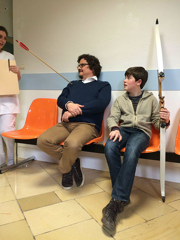 Man with an arrow through sleeve and boy holding a bow sitting in a waiting area, illustrating why women live longer than men.