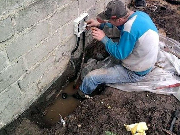 Man performing electrical work in muddy conditions, highlighting risky behavior linked to longevity differences between genders.