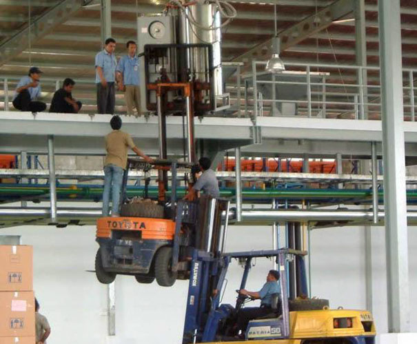 Men using stacked forklifts to lift heavy equipment unsafely, illustrating risk-taking behavior.